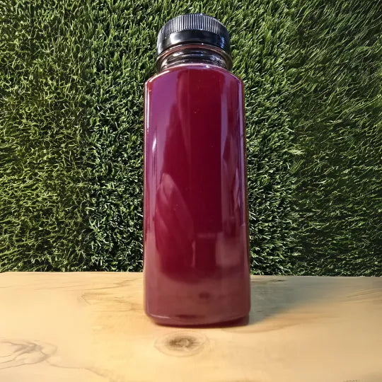 Beet Retreat Cold-Pressed Juice in een doorzichtige fles met een diep paarse kleur, gepresenteerd tegen een natuurlijke achtergrond
