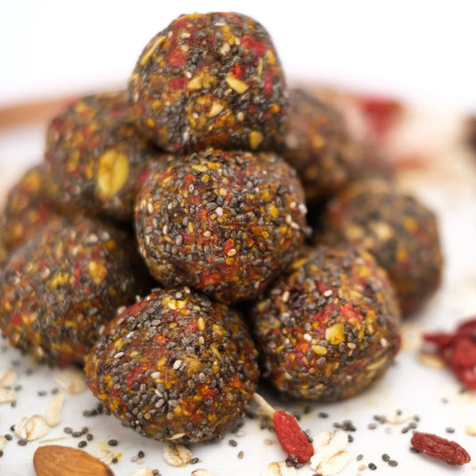 "Goji Almond Bliss Balls, een stapel energierijke bliss balls met gojibessen, amandelen en chiazaad, gepresenteerd op een witte achtergrond met verspreide ingrediΓ«nten."