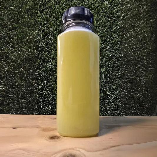 "Een fles 'Refresh' cold-pressed juice van De JuiceDealer, met een lichtgroene kleur, gefotografeerd tegen een achtergrond van kunstgras."