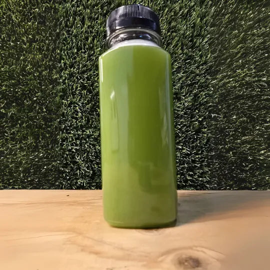 "Tropical Green Cold-Pressed Juice in een doorzichtige fles met een frisse groene kleur, gepresenteerd op een houten ondergrond tegen een groene achtergrond."