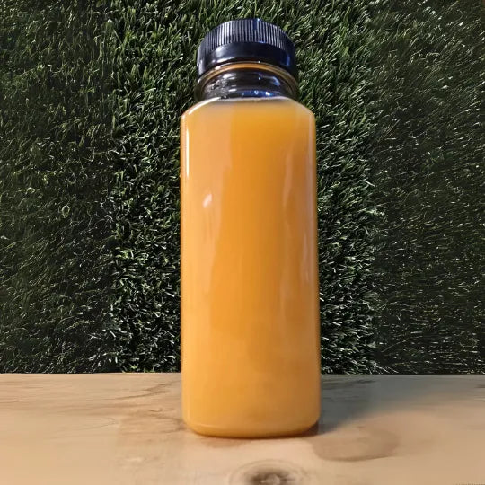 "Fles Orange Pine cold-pressed juice van De JuiceDealer, een verfrissende combinatie van sinaasappel en ananas, gepresenteerd op een houten ondergrond met een natuurlijke achtergrond."