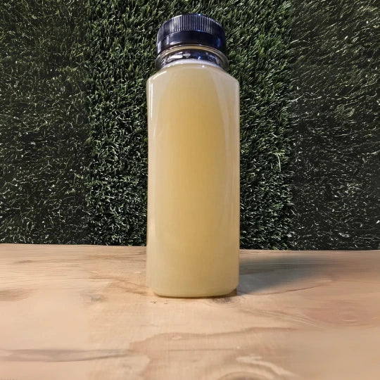 Een verfrissende fles Sweet Detox cold-pressed juice van De JuiceDealer op een houten oppervlak met kunstgras achtergrond."